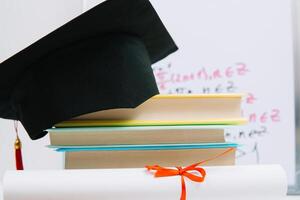 een zwart plein afstuderen hoed met een rood kwast leugens Aan een diploma en een stack van boeken. onderwijs concept foto