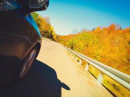 fast motion auto wiel draait snel op asfaltweg met herfst natuur bomen en landschap op kronkelige weg. reizen in de herfst en road trip concept. opzettelijk vervagen filter effect foto