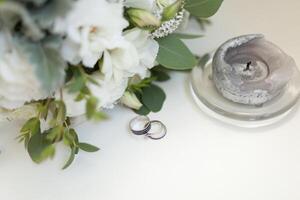 dichtbij omhoog van bruiloft ringen Aan achtergrond van wit bloemen en kaars foto