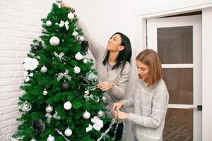 twee jong Dames versieren de Kerstmis boom, voorbereidingen treffen voor de nieuw jaar viering foto