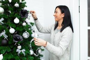 een jong vrouw versieren de Kerstmis boom, voorbereidingen treffen voor de nieuw jaar viering foto