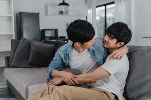 jong aziatisch homopaar knuffel en kus thuis. aantrekkelijke aziatische lgbtq-trots mannen gelukkig ontspannen brengen romantische tijd samen door terwijl ze op de bank liggen in het woonkamerconcept. foto