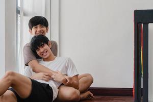 Aziatische homo paar liegen en knuffelen op de vloer thuis. jonge aziatische lgbtq-mannen zoenen gelukkig ontspannen rust samen brengen romantische tijd door in de woonkamer met regenboogvlag in het moderne huis in de ochtend. foto