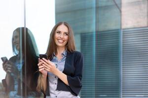 bedrijf vrouw 35 jaren gekleed streep overhemd en zwart jasje met lang haar- staand in de buurt kantoor gebouw buitenshuis gebruik smartphone foto