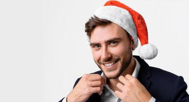 jong knap Kaukasisch vent in bedrijf pak en de kerstman hoeden staat Aan wit achtergrond in studio en tanden smilie foto