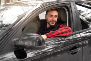 jong aantrekkelijk Kaukasisch Mens zit Bij de wiel van zijn auto zonnig winter dag. foto