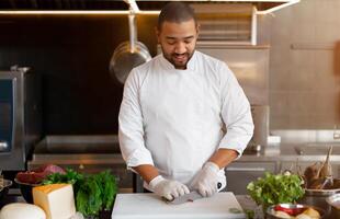 knap jong Afrikaanse chef staand in professioneel keuken in restaurant voorbereidingen treffen een maaltijd van vlees en kaas groenten. foto