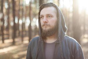 dichtbij omhoog portret van een gebaard hipster toerist in grijs kap Mens in de zonlicht bossen Woud foto