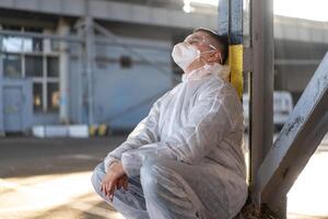 wanhoop gezondheidszorg arbeider in wit covid beschermend overall. moe mannetje Kaukasisch dokter grijpt zijn hoofd ineenkrimpen in depressie gedurende coronavirus pandemisch foto
