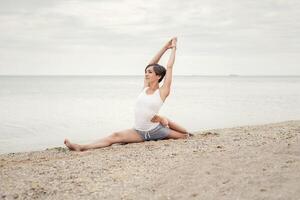 mooi meisje beoefenen yoga Aan de strand in de buurt de zee. zit Aan een touw, doet een uitrekken. foto