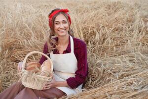 vrouw boer zittend tarwe agrarisch veld- vrouw bakker Holding rieten mand brood Product foto