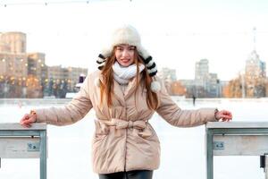 mooi lief jong volwassen vrouw brunet haar- warm winter jassen staat in de buurt ijs vleet baan achtergrond stad- vierkant. Kerstmis humeur levensstijl foto