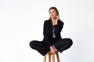 jong modieus bedrijf vrouw zittend hoog bar houten stoel lotus houding gekleed zwart kantoor pak geïsoleerd in wit achtergrond foto
