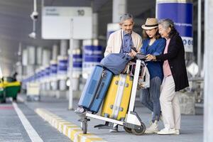 groep van Aziatisch familie toerist passagier met senior is gebruik makend van mobiel toepassing naar telefoontje plukken omhoog taxi Bij luchthaven terminal voor vervoer gedurende hun vakantie reizen en lang weekend vakantie foto