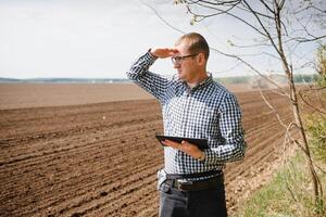 boer in veld- onderzoeken zaaien en Holding tablet in zijn handen. foto