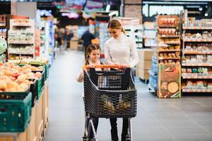 mooi moeder Holding kruidenier mand met haar kind wandelen in supermarkt. boodschappen doen voor gezond. foto