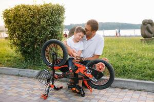 gelukkig vader en zijn zoon hebben pret samen Bij de groen park, vaststelling fiets samen. vader dag. foto