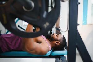 gewicht lifter Bij de bank druk op hijs- een barbell Aan een bank. foto