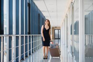 elegant vrouw in een zwart jurk met een koffer in de luchthaven terminal aan het wachten voor een vlak. foto