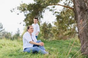 gelukkig familie moeder met zoon kind spelen hebben pret samen Aan de gras in zonnig zomer dag, leven moment foto