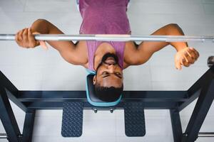 gewicht lifter Bij de bank druk op hijs- een barbell Aan een bank. foto