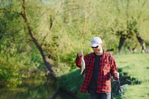 visser door de rivier- met een vangst van vis. Mens visser houdt in hand- vis. foto