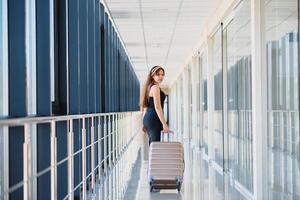 voorkant visie van een reiziger vrouw wandelen draag- een koffer in een luchthaven gang foto