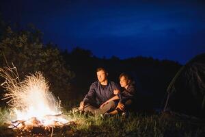 gelukkig romantisch paar reizigers resting Bij vreugdevuur in de buurt gloeiend toerist tent onder verbazingwekkend nacht lucht. de concept van actief recreatie en reizen met een tent foto