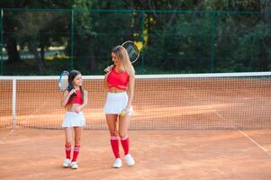 weinig meisje en haar moeder spelen tennis Aan rechtbank foto