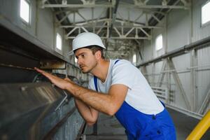 glimlachen en gelukkig medewerker. industrieel arbeider binnenshuis in fabriek. jong technicus met wit moeilijk hoed. foto