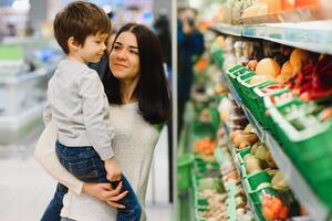 vrouw en kind jongen gedurende familie boodschappen doen met trolley Bij supermarkt foto