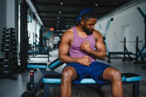 zwart atleet buigen spieren, demonstreren sterk biceps in Sportschool foto