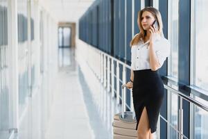 portret van jong aantrekkelijk zakenvrouw pratend Aan smartphone met haar koffer in luchthaven foto