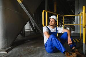 glimlachen en gelukkig medewerker. industrieel arbeider binnenshuis in fabriek. jong technicus met wit moeilijk hoed. foto