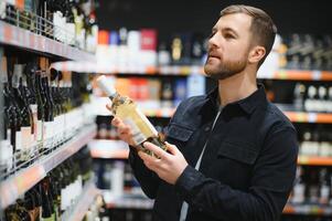 portret van jong blij positief mannetje klant selecteren wijn in supermarkt foto