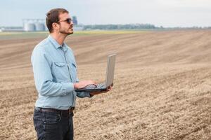 gelukkig boer met laptop staand in tarwe veld- in voorkant van graan silo foto