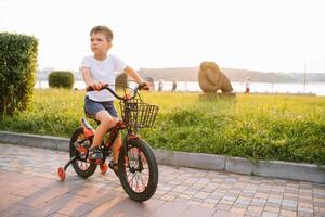 kinderen Aan een fiets Bij asfalt weg in vroeg ochtend. weinig jongen leert naar rijden een fiets in de park. gelukkig glimlachen kind, rijden een wielersport. foto