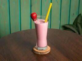 een glas van aardbei smoothie schudden met rauw aardbei en rietje geïsoleerd Aan houten tafel kant visie gezond drinken voor vitamine c foto