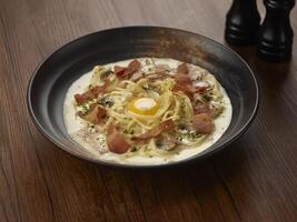 kip Carbonara met kalkoen spek pasta in een schotel geïsoleerd Aan donker houten tafel kant visie Singapore voedsel foto