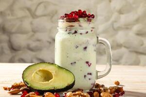 avocado milkshake met noten, granaatappel zaden, okkernoot, amandel en cachou geserveerd in pot geïsoleerd Aan achtergrond top visie van gezond ochtend- drinken foto