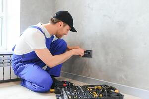 bouw arbeider elektricien assembleert een elektrisch stopcontact in een appartement foto