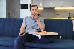 eet pizza terwijl aan het kijken TV show. Mens met baard binnenshuis. foto
