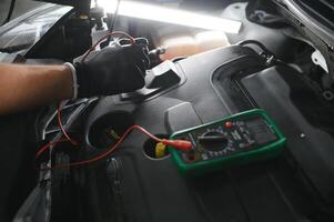 auto monteur is gebruik makend van een multimeter met Spanning reeks meting naar controleren de Spanning niveau van de auto accu. foto