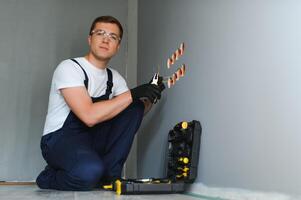 elektricien bouwer Bij werk, installatie van stopcontacten en schakelaars. professioneel in overall met een elektricien hulpmiddel. tegen de achtergrond van de reparatie plaats. foto