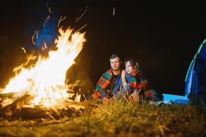 gelukkig romantisch paar reizigers resting Bij vreugdevuur in de buurt gloeiend toerist tent onder verbazingwekkend nacht lucht. de concept van actief recreatie en reizen met een tent foto