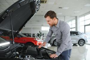 looks onder de kap van auto. jong Mens in de auto dealerschap. foto