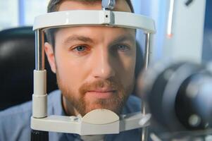 volwassen Mens gezichtsvermogen test met verrekijker spleetlamp. controle netvlies van een mannetje oog detailopname. oogheelkunde kliniek foto