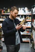 portret van jong blij positief mannetje klant selecteren wijn in supermarkt foto