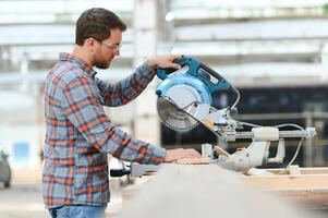 hout snijdend tafel met elektrisch circulaire zaag. professioneel timmerman in uniform snijdend houten bord Bij zagerij timmerwerk fabricage . zagen machine foto