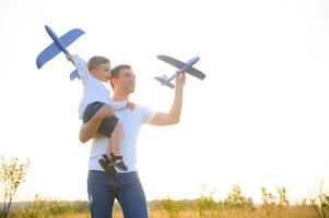 schattig weinig jongen en zijn knap jong vader zijn glimlachen terwijl spelen met een speelgoed- vliegtuig in de park. foto